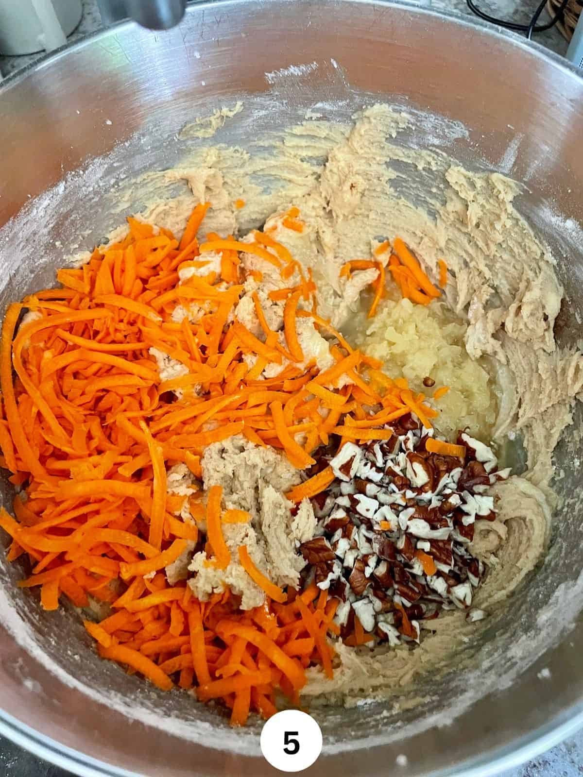 Shredded carrots, Chopped pecans, and crushed pineapple on top of some cake batter in a stainless steel mixing bowl.