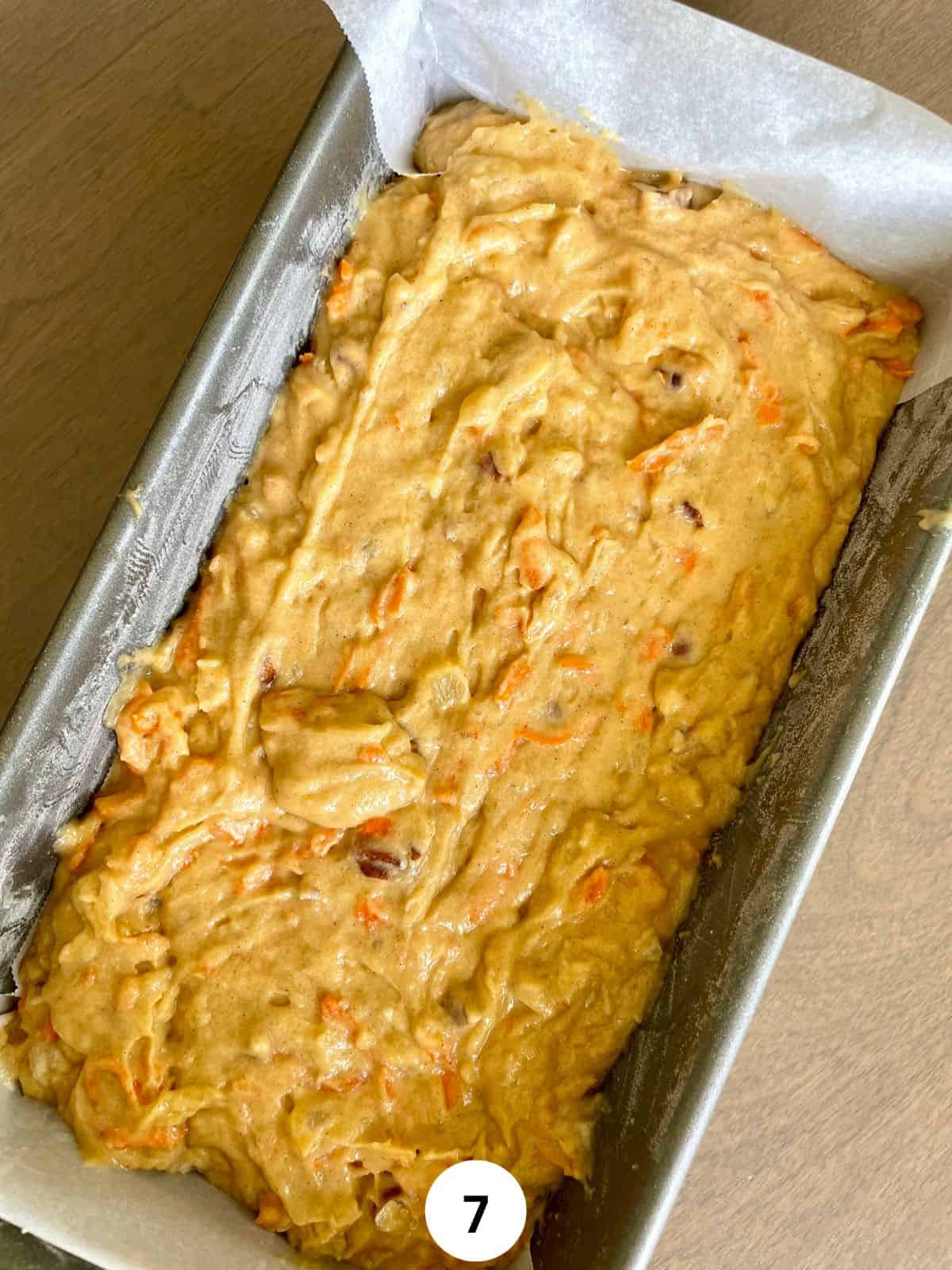 Carrot cake batter in a parchment-lined metallic loaf pan.