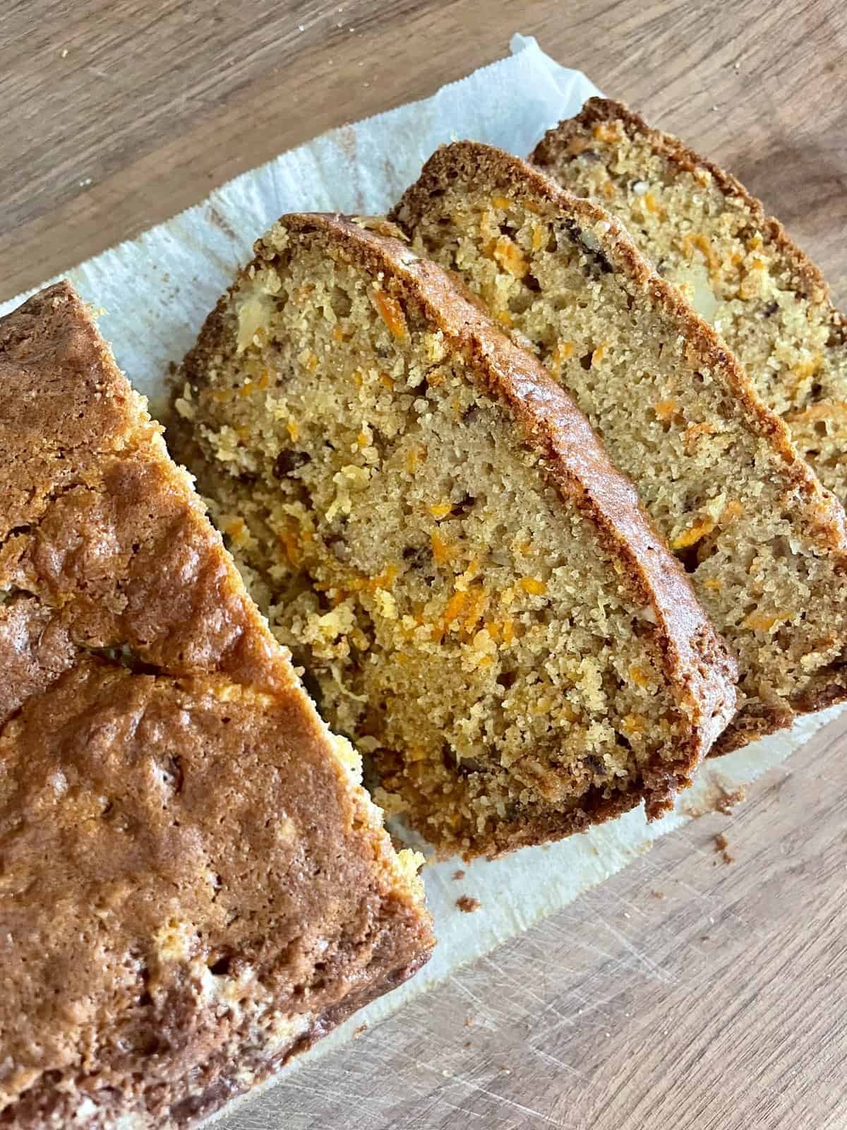 Sliced carrot cake on parchment paper kept on a wooden chopping board.