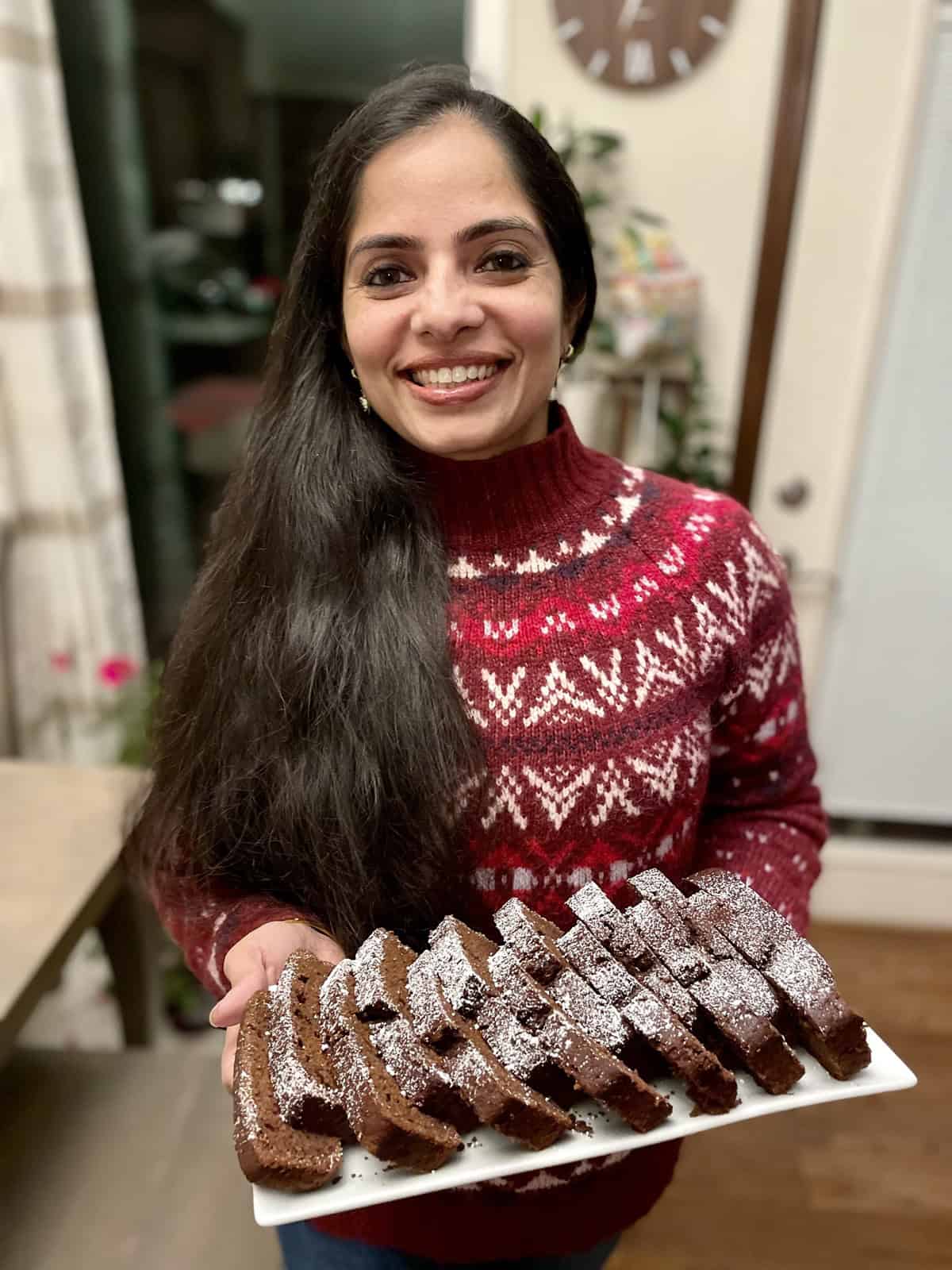 Vaishali standing with a platter of sliced mocha loaf cake in her hands.