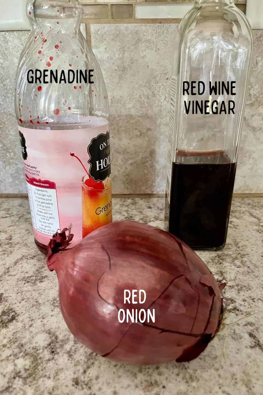 A red onion, a bottle of grenadine, and a bottle of red wine vinegar on a kitchen counter.