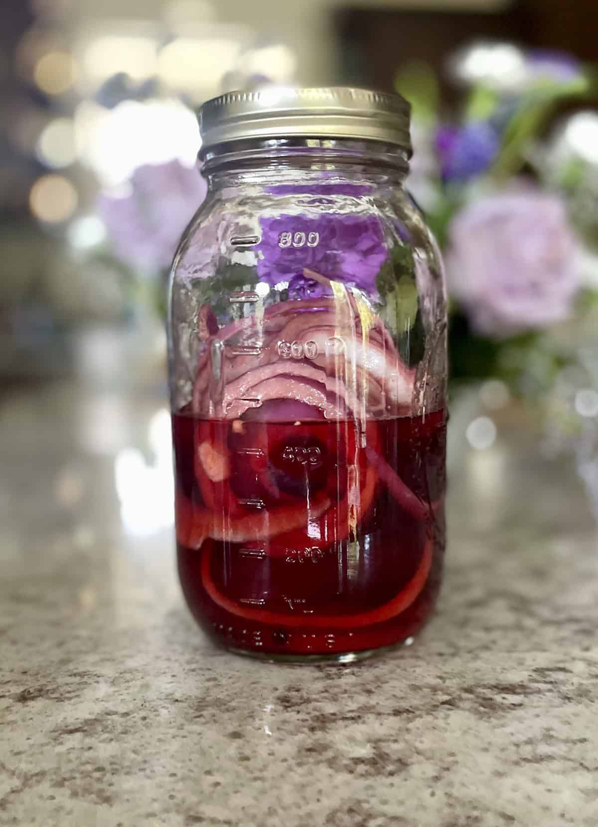 Pickled red onions with the pickling liquid in a glass mason jar kept on a kitchen counter.
