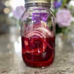 Pickled red onions with the pickling liquid in a glass mason jar kept on a kitchen counter.