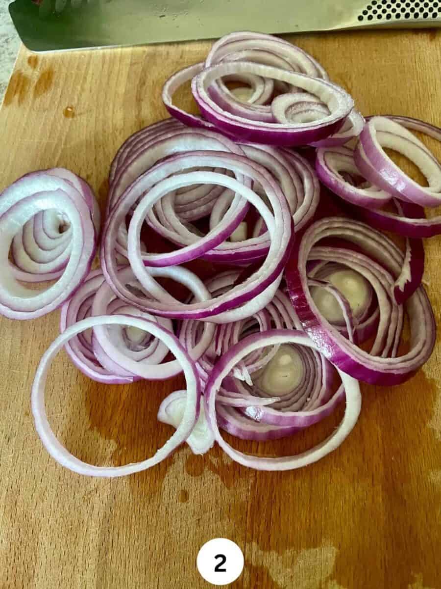 Sliced red onions on a wooden chopping board.