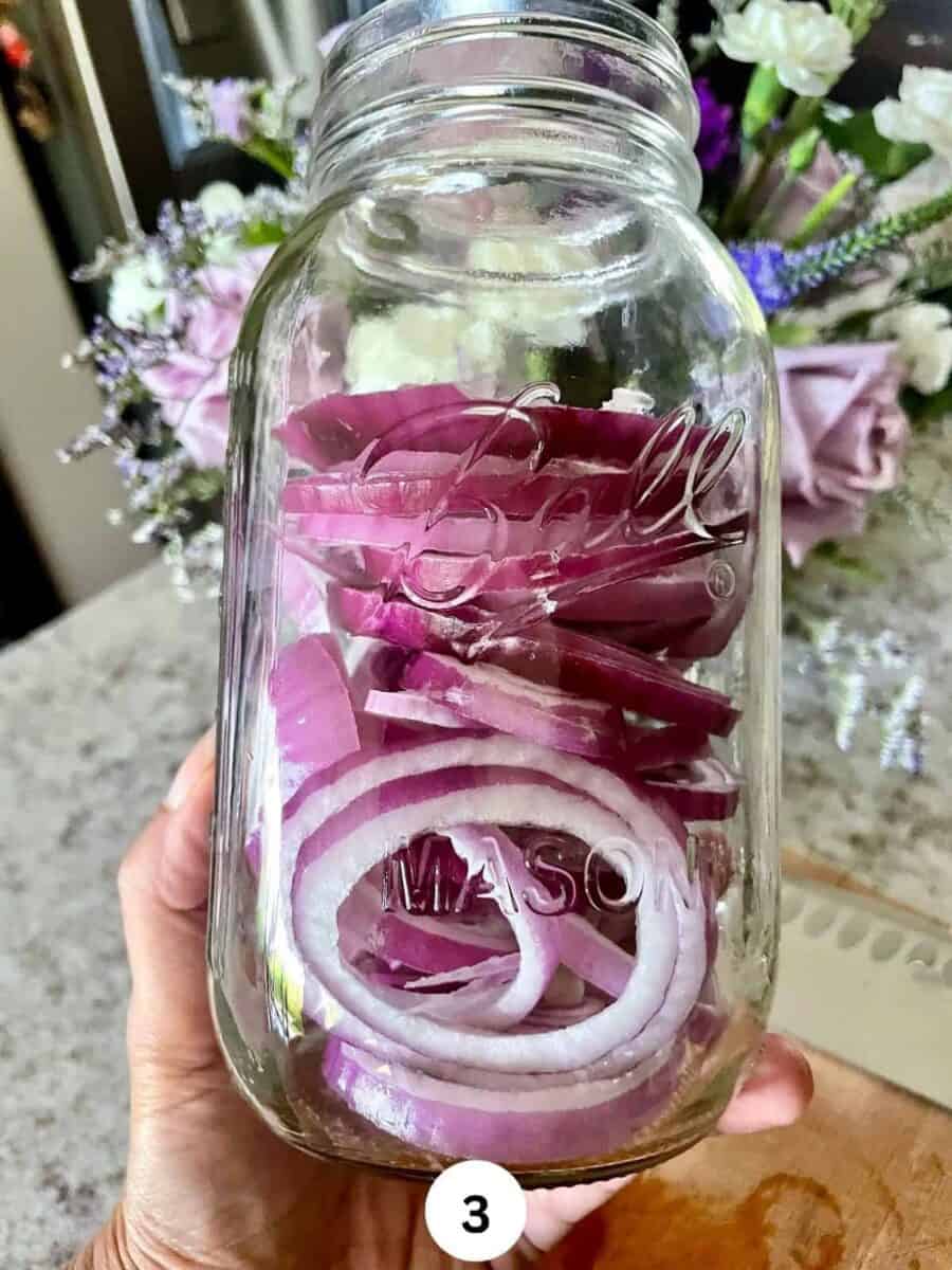 Sliced red onions in a glass mason jar held in a hand.