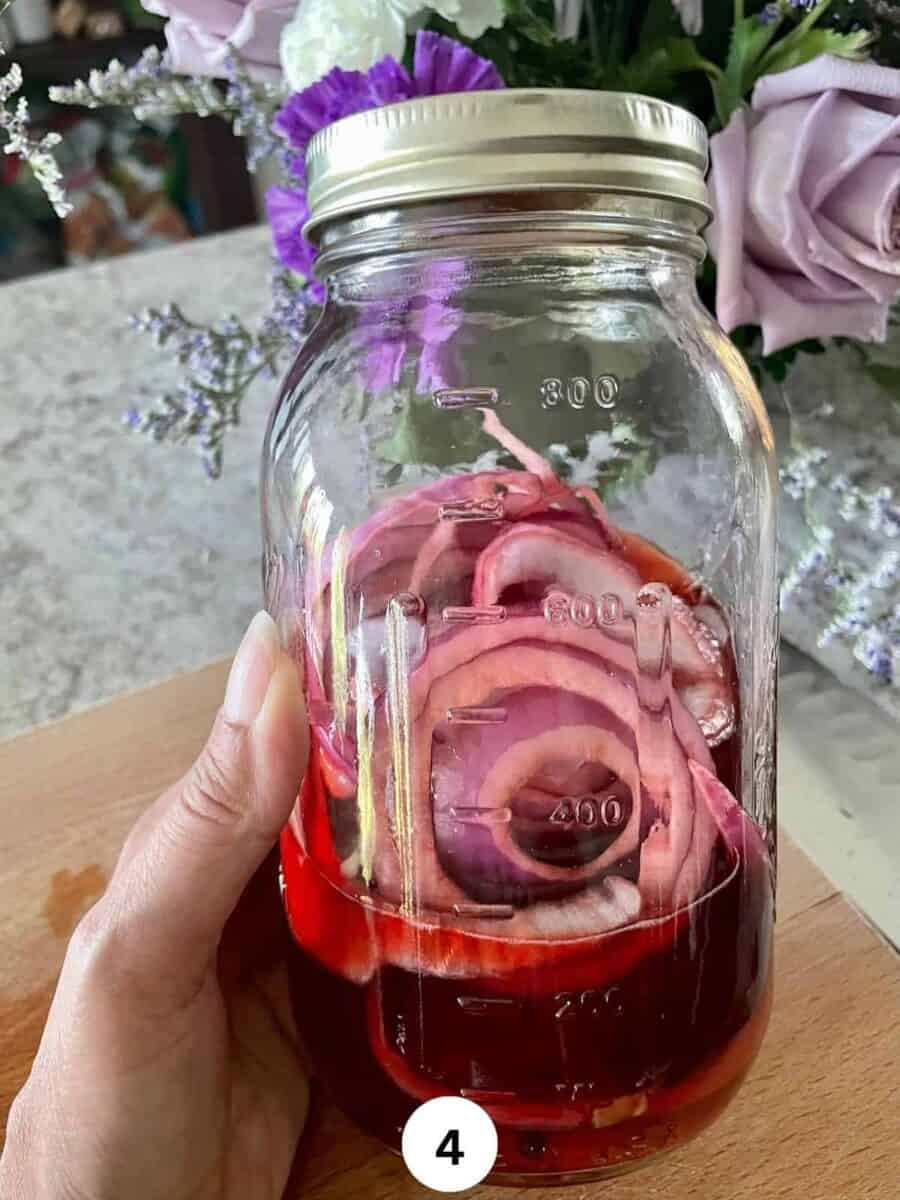 Sliced red onions with red pickling liquid in a glass mason jar held in a hand.