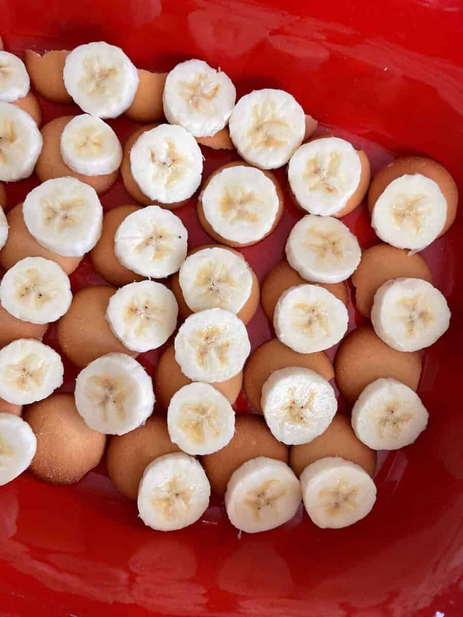 Slices of peeled bananas layered over vanilla wafers in a red ceramic dish.