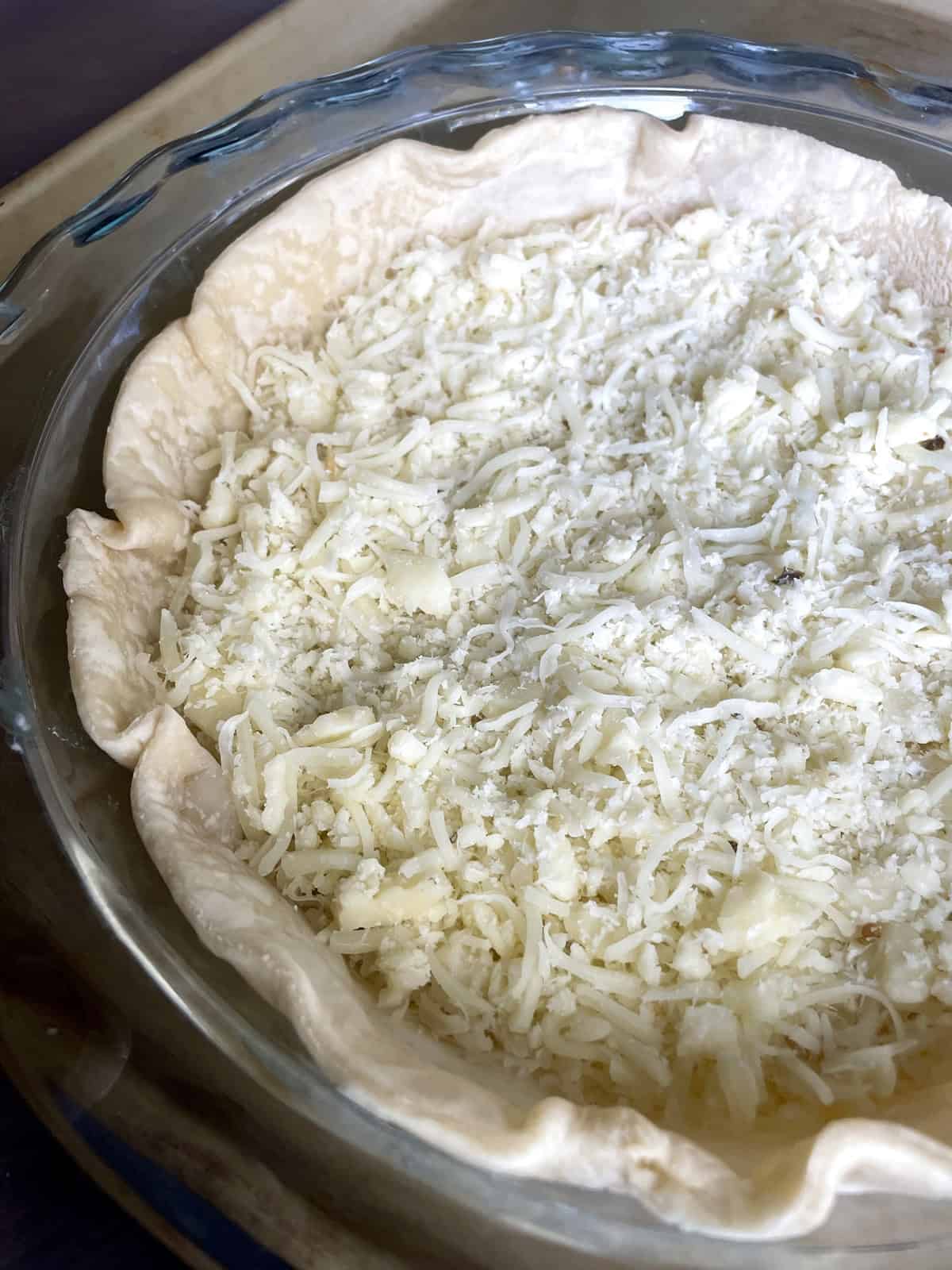 A glass pie dish filled with pie crust and grated cheese.