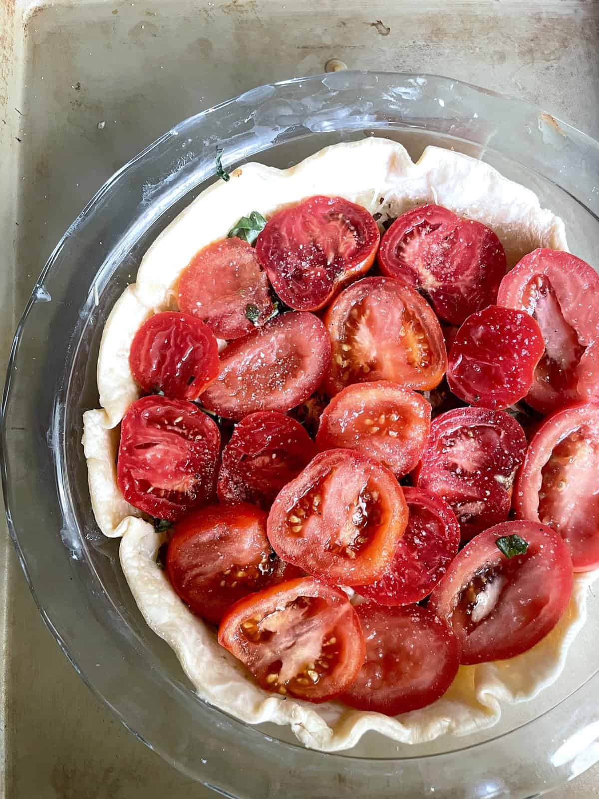 A glass pie dish filled with pie crust and sliced tomatoes.