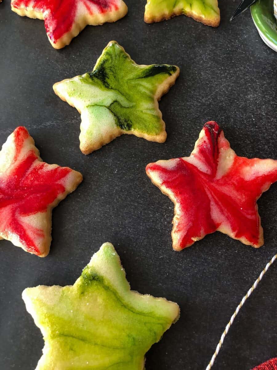 Star-shaped cutout lemon sugar cookies with red, green, and white glaze on a black background.