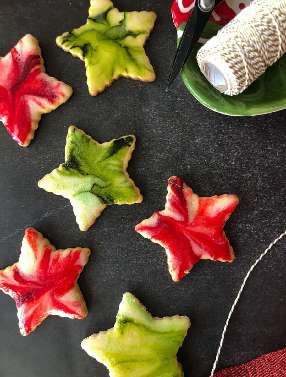 Star-shaped cutout lemon sugar cookies with red, green, and white glaze on a black background. A spool of twine is on one side.