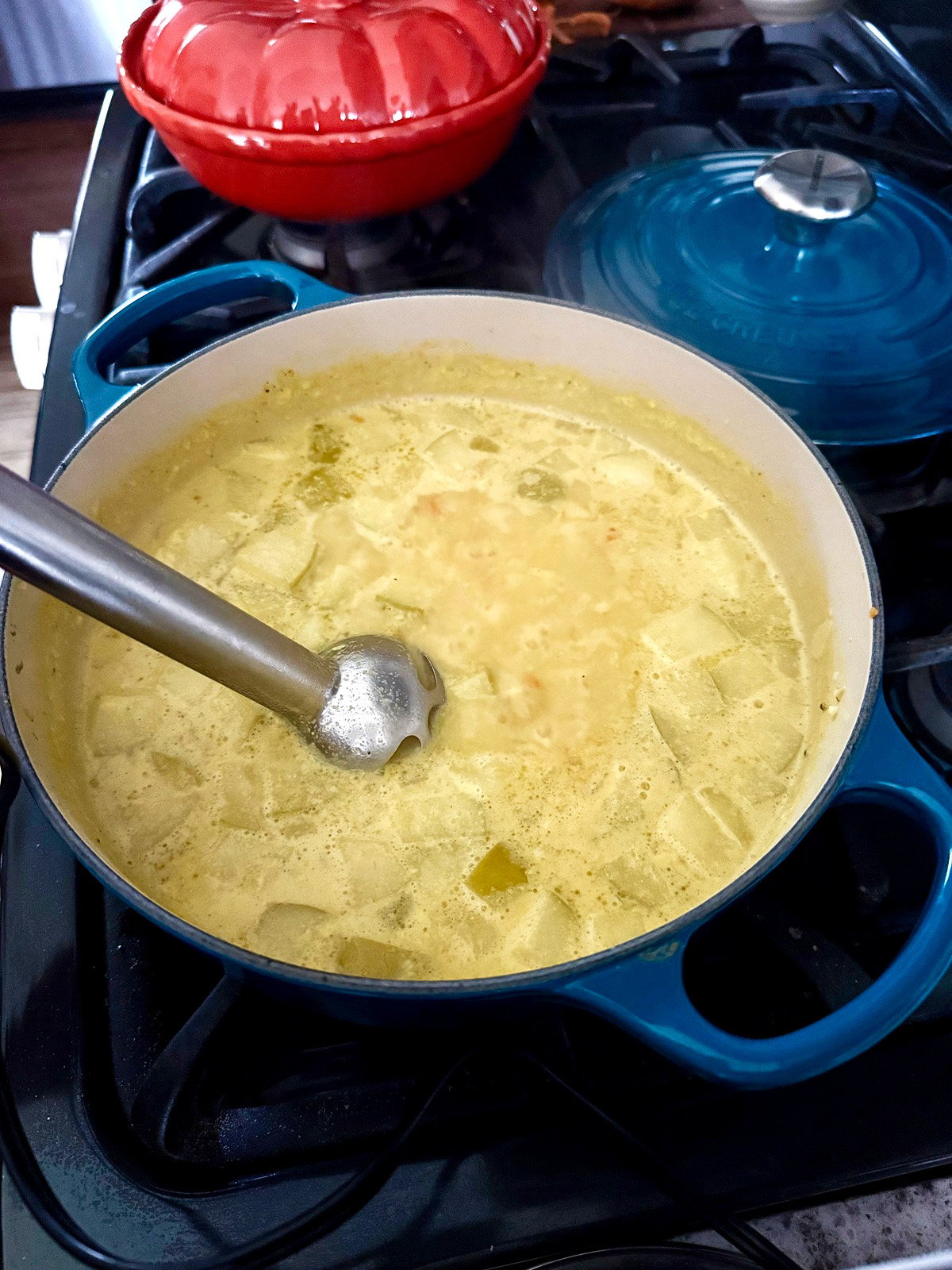 Apple harvest soup getting blended with an immersion hand blender in a blue enameled cast iron soup pot.