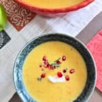 Fall apple harvest soup in a blue ceramic bowl topped with a dollop of sour cream, pomegranate, and rosemary.
