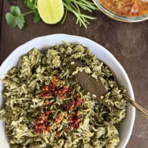 Spinach Rice with Chili crisp in a white ceramic bowl on a dark metallic background with a sliced lime, cilantro sprigs, and a bowl of curry.