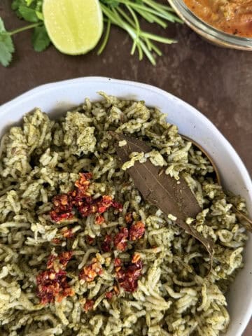 Spinach Rice with Chili crisp in a white ceramic bowl on a dark metallic background with a sliced lime, cilantro sprigs, and a bowl of curry.
