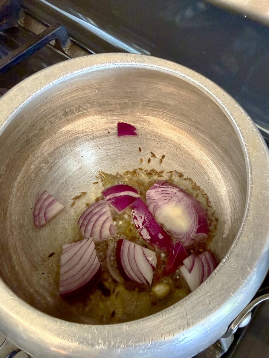A pot with chopped re onions in oil with cumin seeds in it.