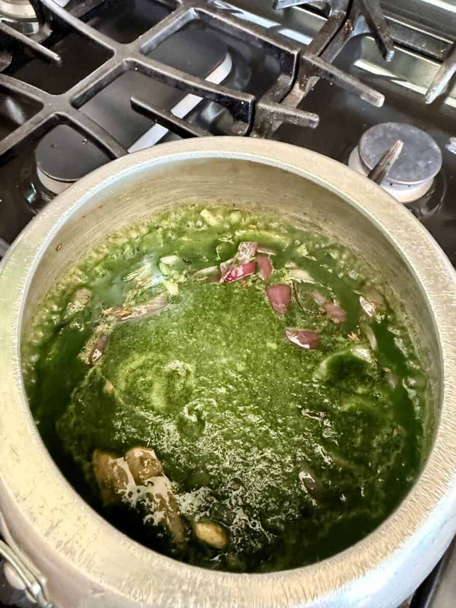 A pot on a stove with spinach puree and rice in it. There are some chopped red onions in it.