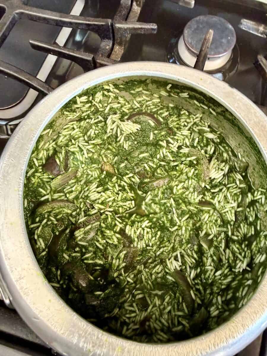 An aluminum pot on a stove with rice and green broth in it.
