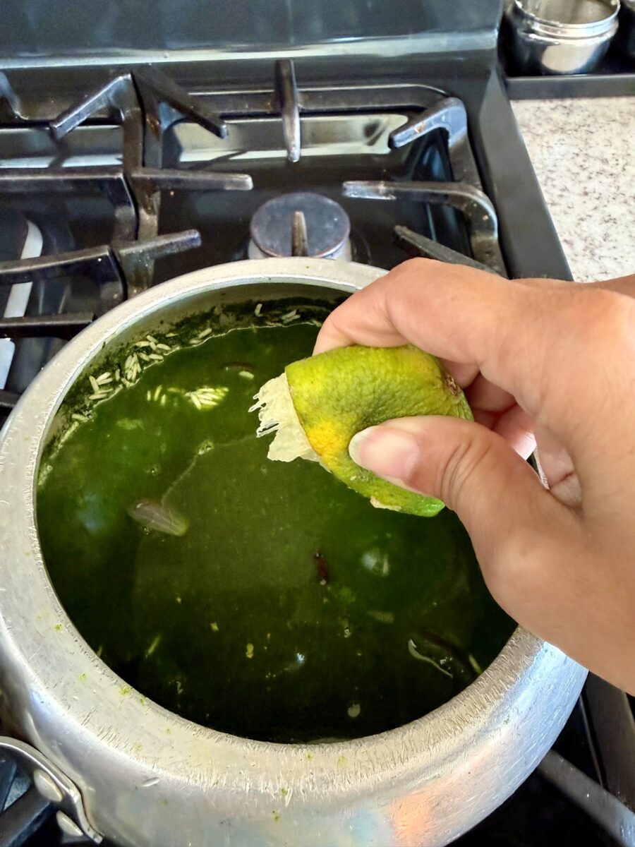 A hand squeezing a lime on top of a pot with green colored broth in it.
