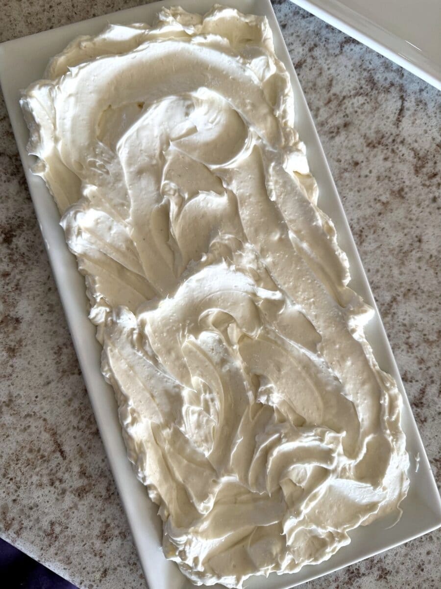 Whipped cream cheese spread on a rectangular white ceramic platter set on a white and grey countertop.