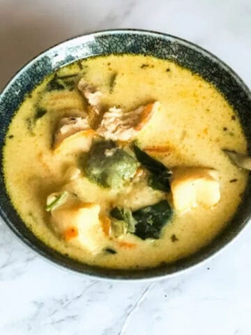 Chicken Gnocchi soup in a blue ceramic bowl on a white marble background.
