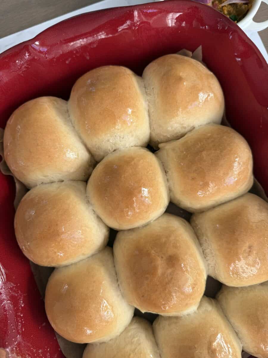 Rows of baked dinner rolls in a red ceramic baking dish.