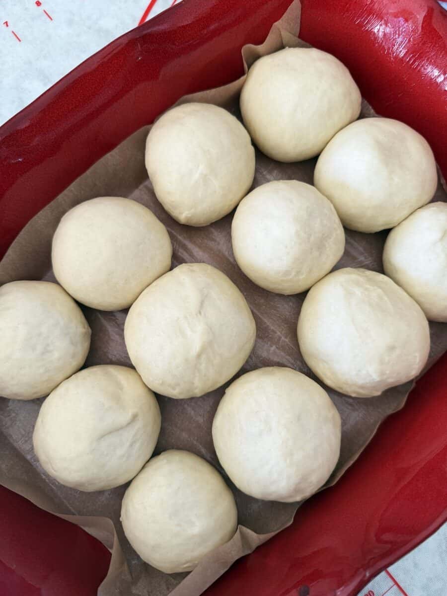 Dough balls arranged in rows on a parchment lined red ceramic baking dish.