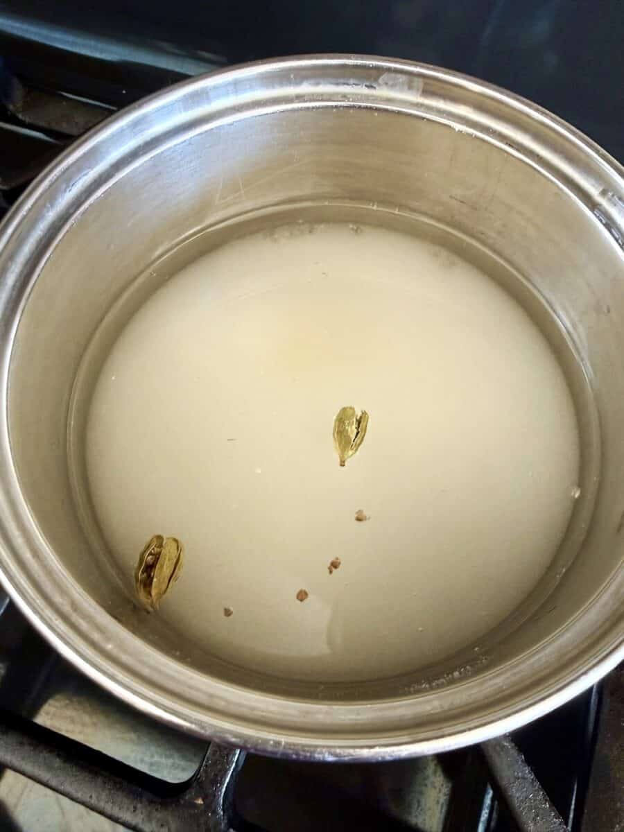 Water, sugar, and green cardamom pods and seeds in a stainless steel sauce pan.