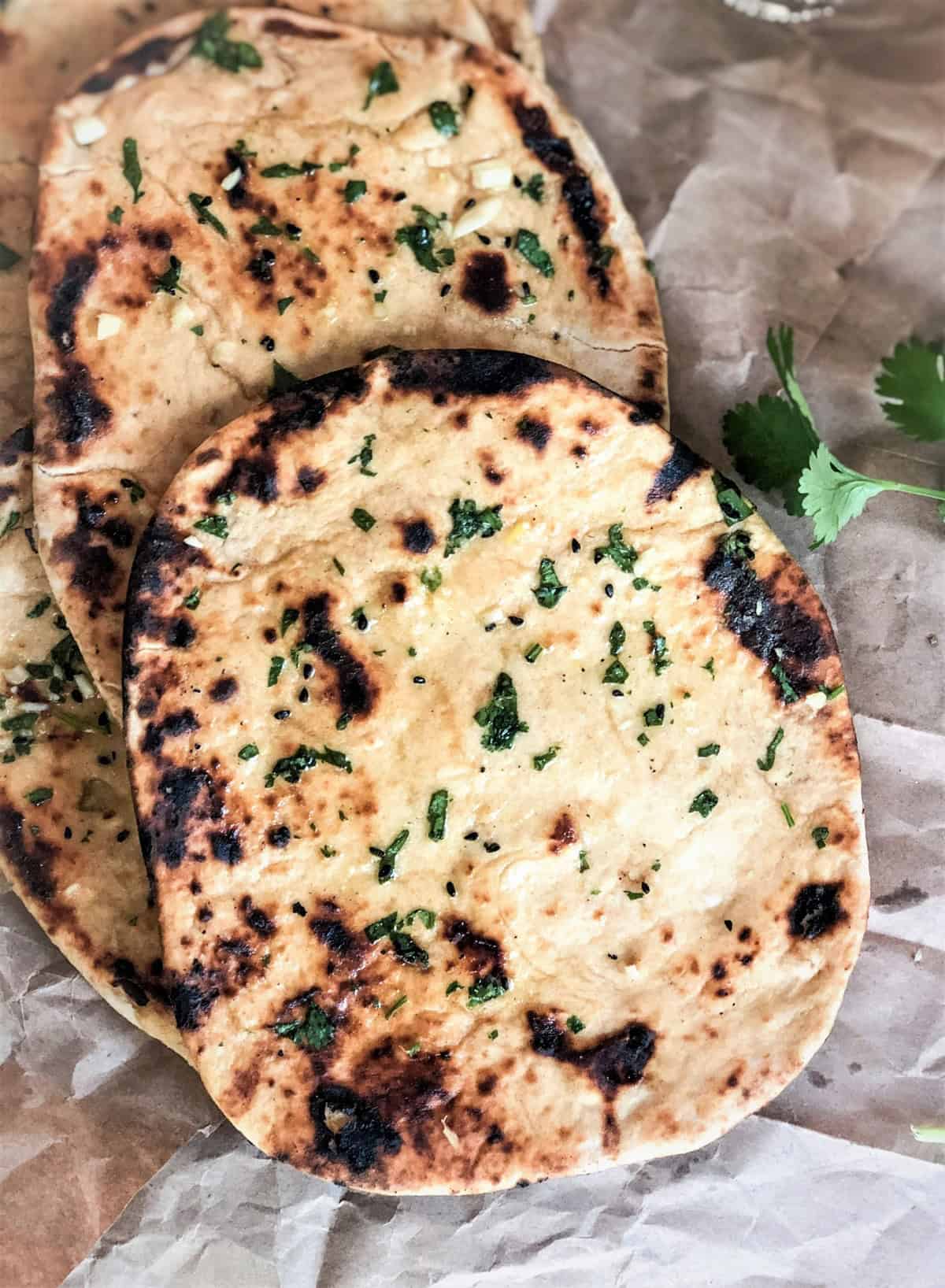 Garlic Naan bread with herbs, pickled onions, and chutney, served on a rustic surface. Ideal for Indian meals.