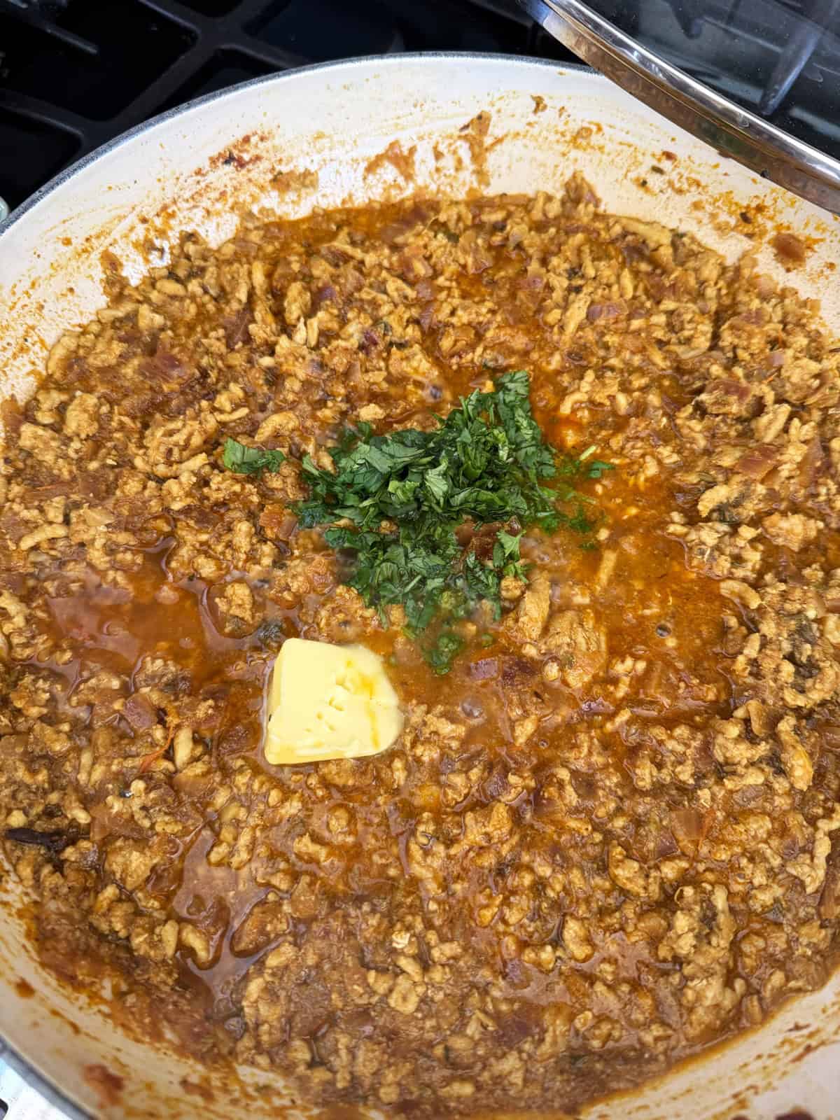 Ground meat curry in a pan with chopped cilantro and a pat of butter.