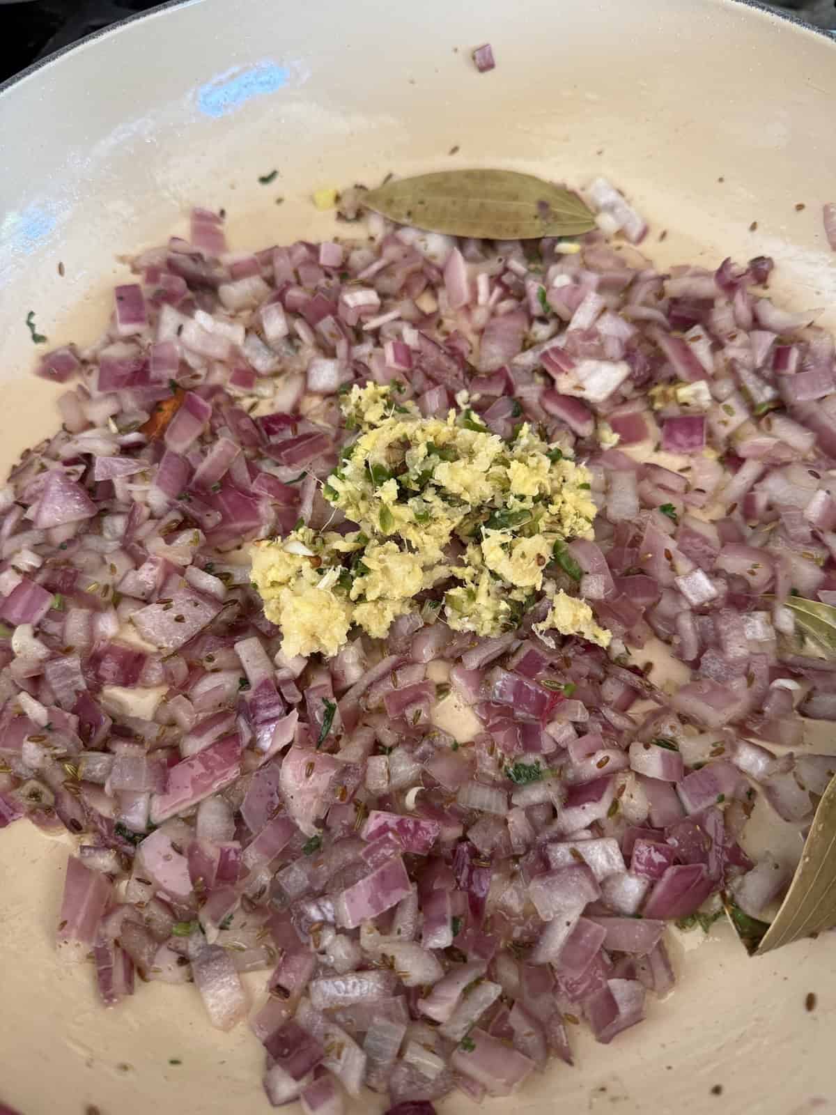 Chopped onions cooking in a pan with ginger garlic and green chili paste.