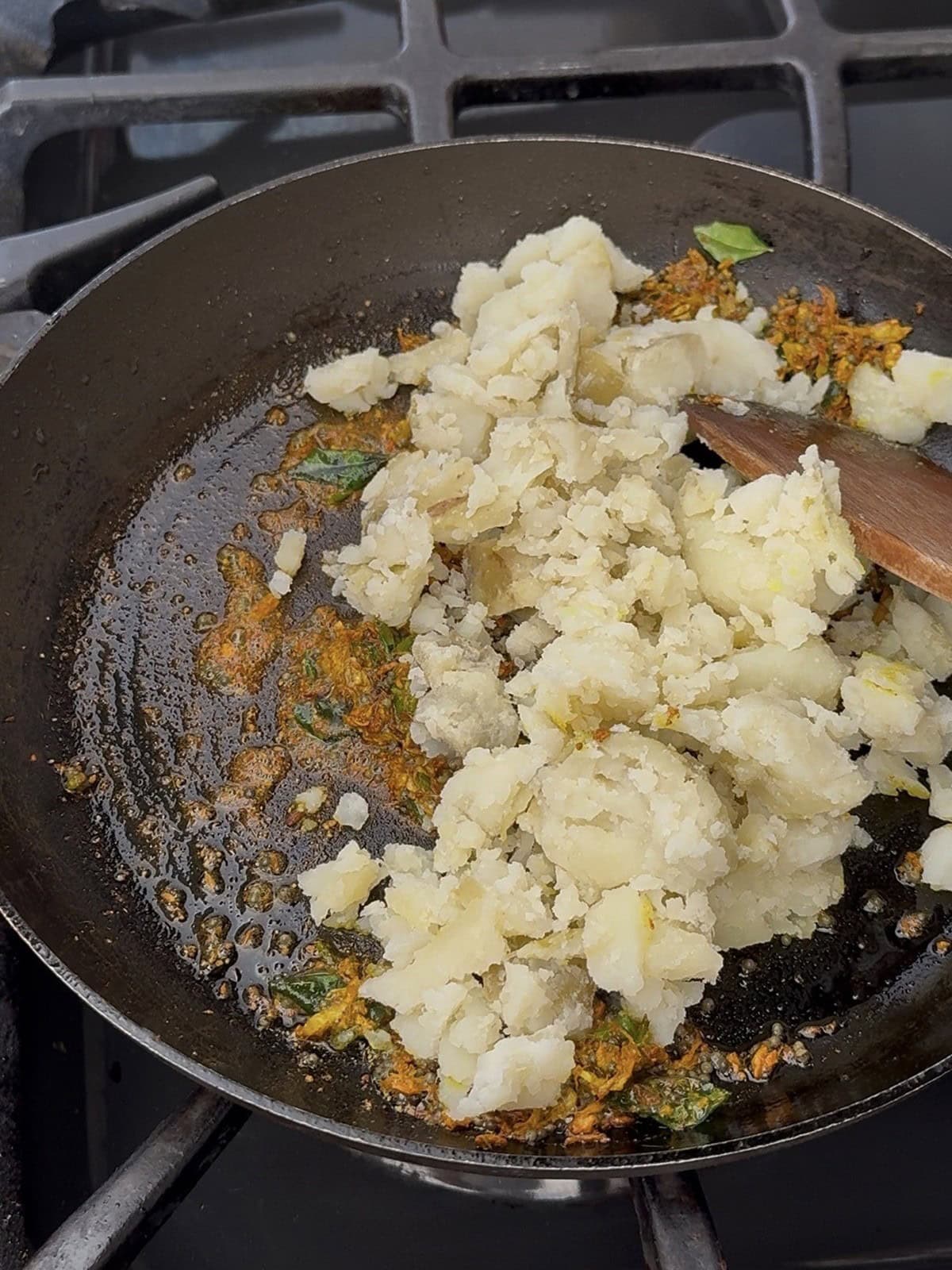 Mashed potatoes being prepared in a skillet with herbs and spices.