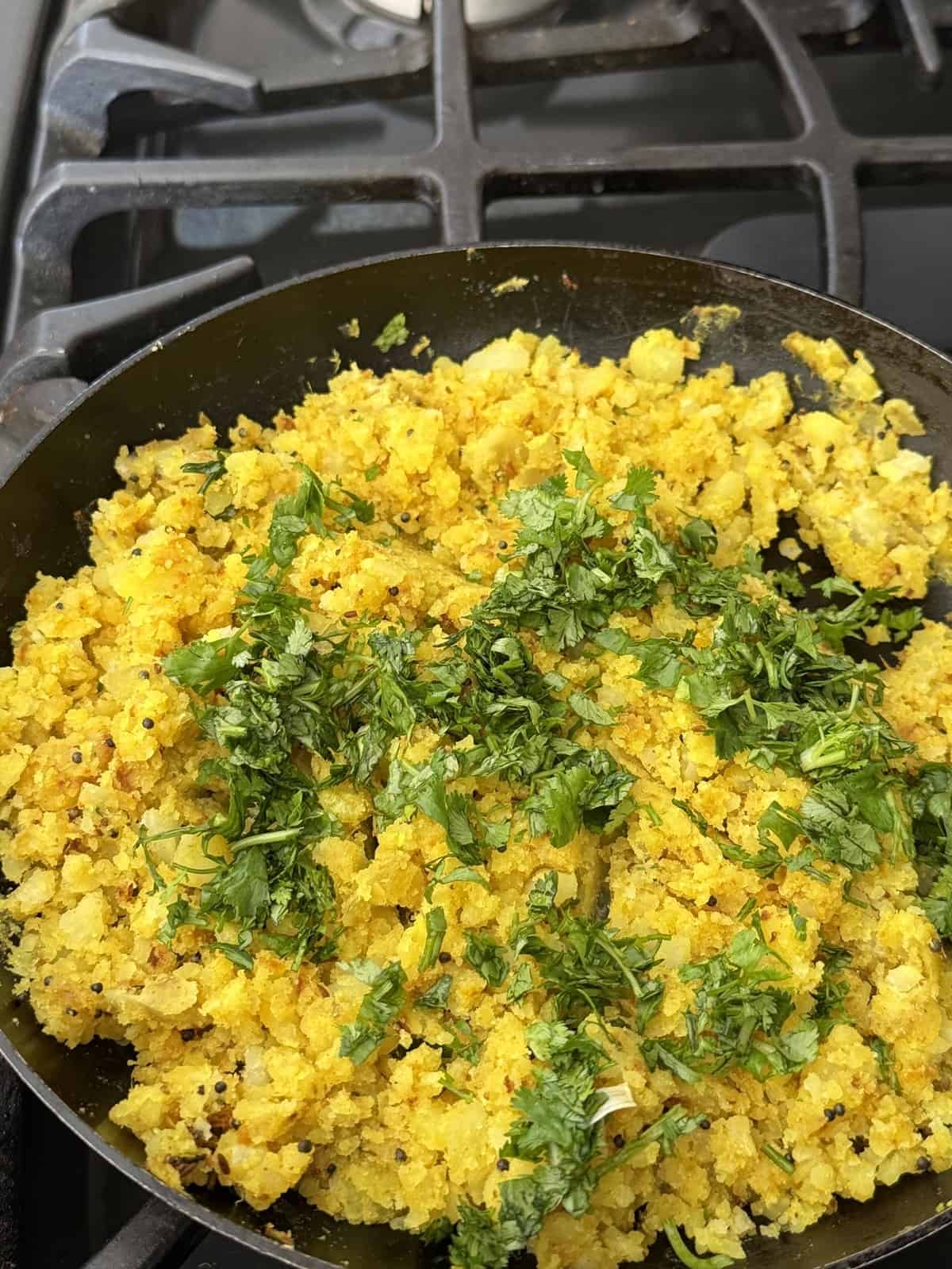 Spiced mashed potatoes garnished with chopped cilantro in a frying pan.