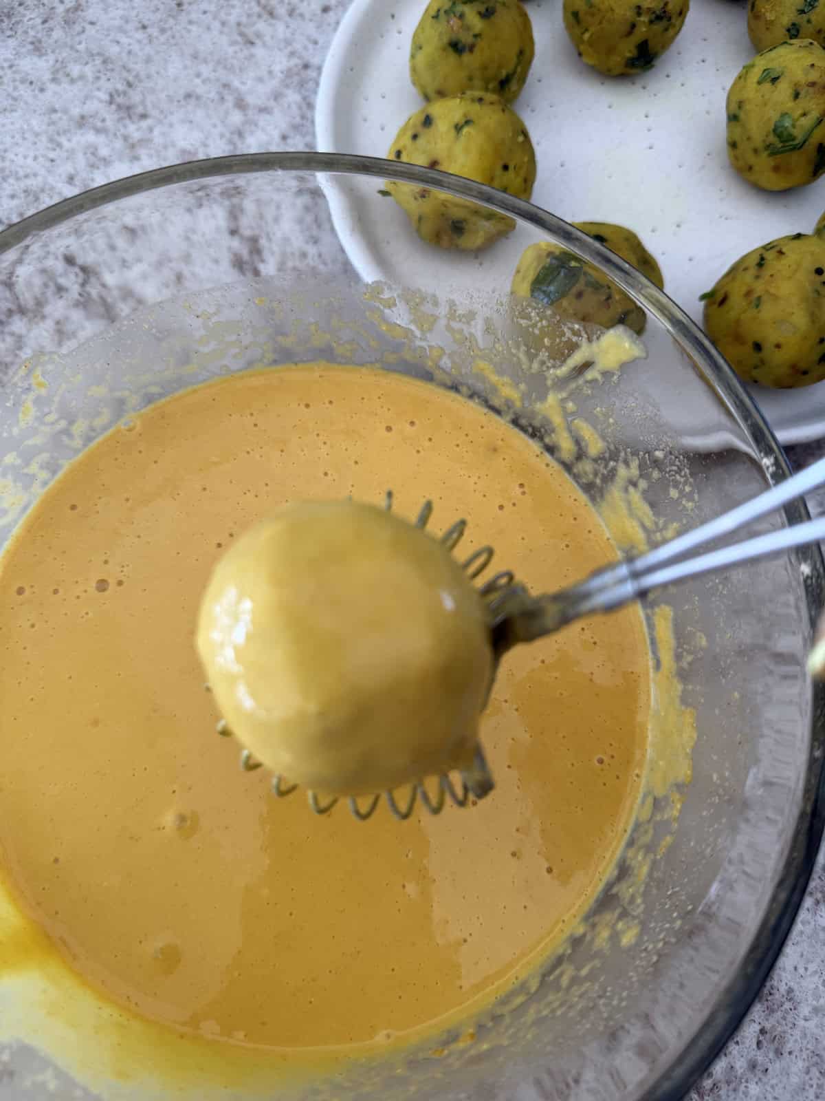 Delicious homemade mashed potato balls being prepared with vibrant yellow chickpea flour batter.