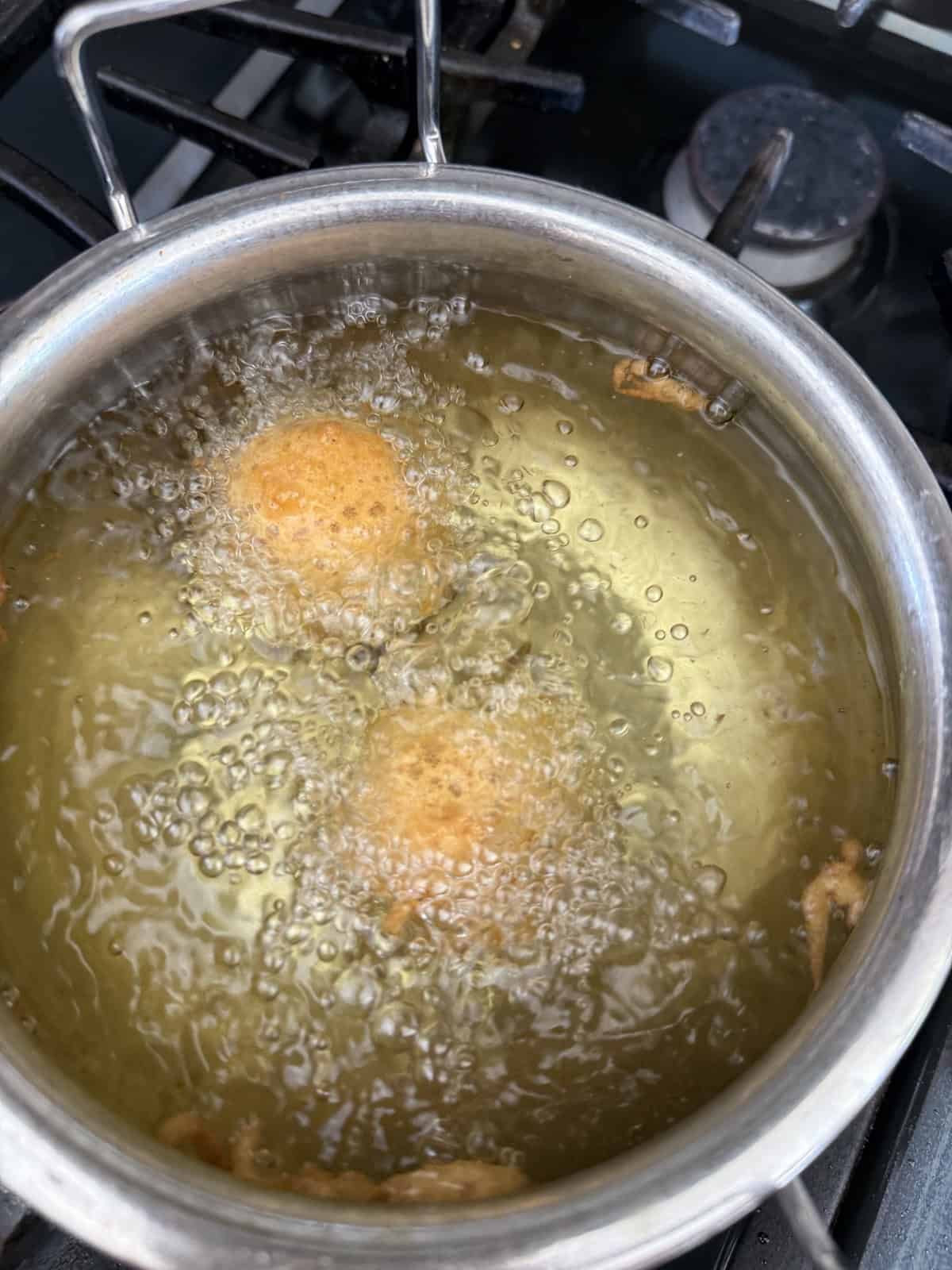 Batata vada frying in oil in a stainless steel pan in kitchen setting.