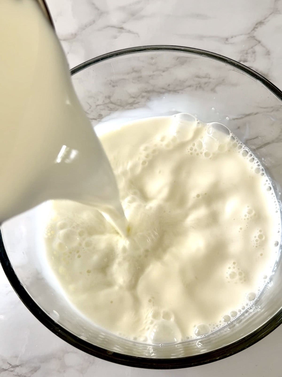 Pouring milk into a glass bowl to make homemade dahi or Indian yogurt.