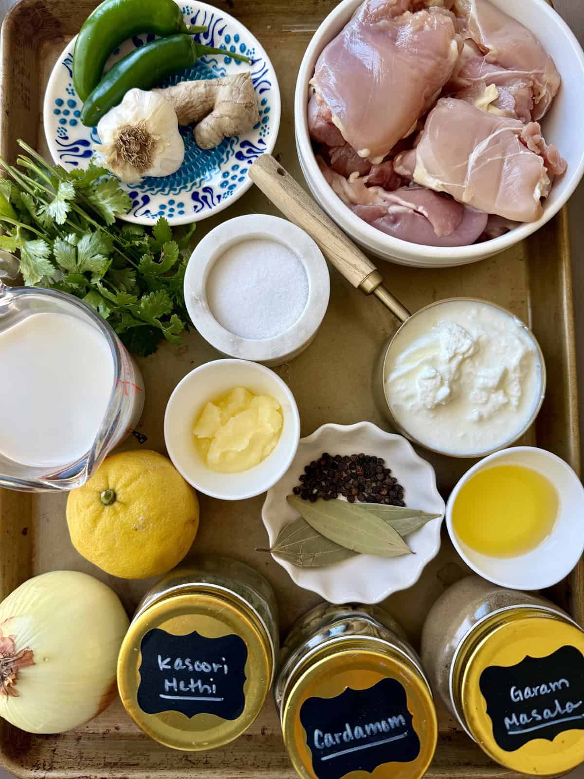 Ingredients for making Afghani Chicken recipe without cashews, including raw chicken, cilantro, ghee, spices, onion, lemon, green chili, yogurt, and heavy cream.