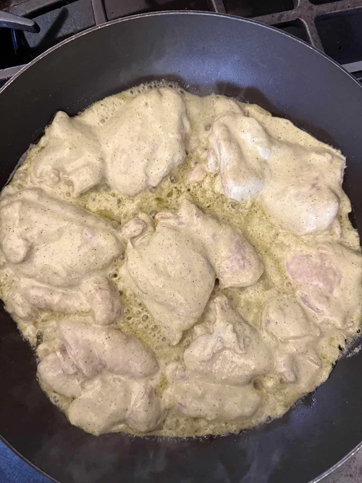 Chicken pieces cooking in a skillet with Afgani marinade without cashews.