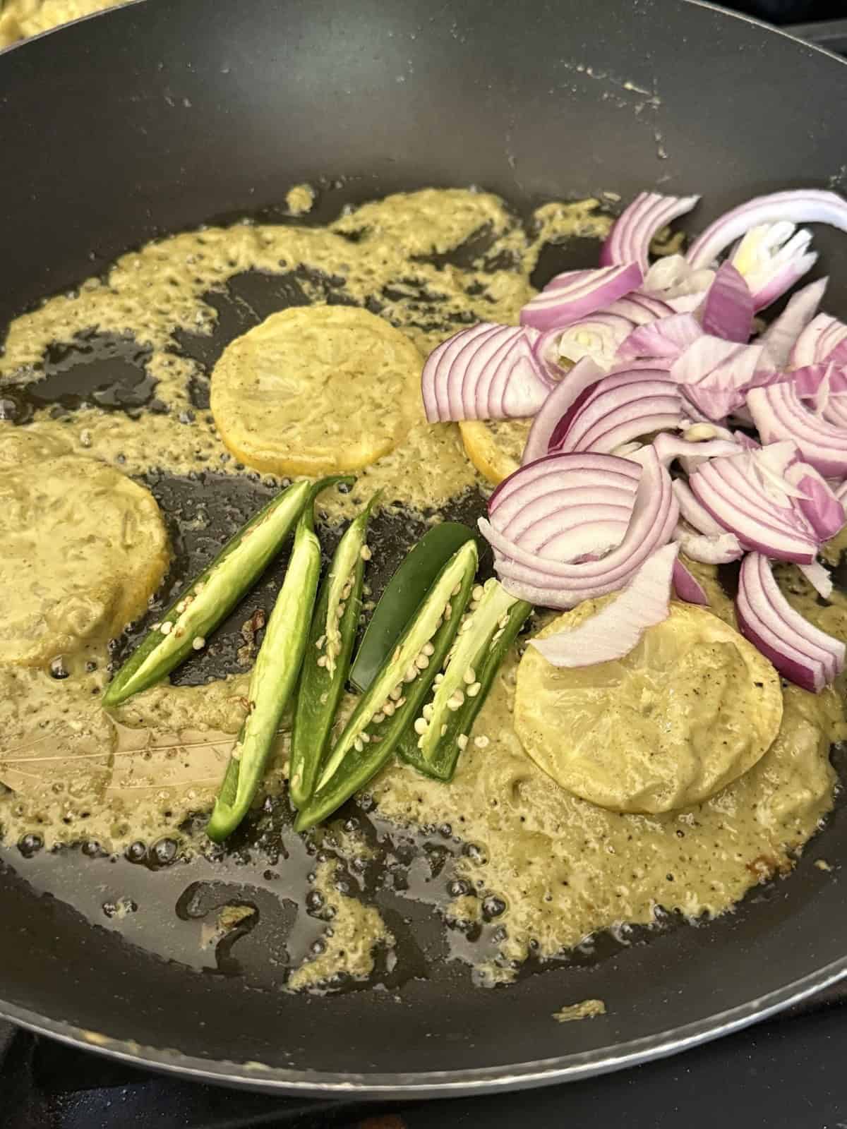 Sliced onions, lemon slices, and green chilies in a non-stick skillet.