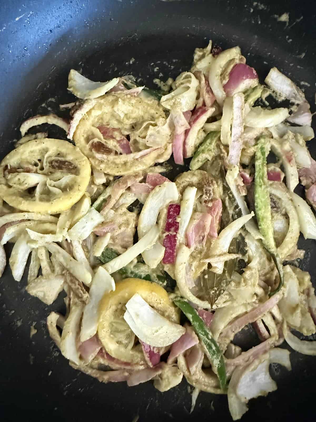 Sautéed sliced onions, lemon slices, and green chilies with bay leaves and raisins in a non-stick skillet.