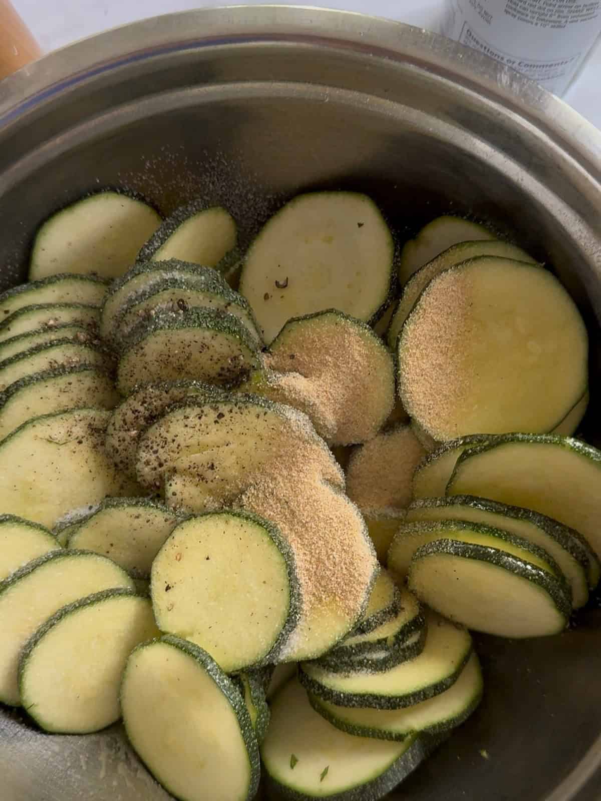 Zucchini slices seasoned with spices in a metal bowl for cooking or baking.