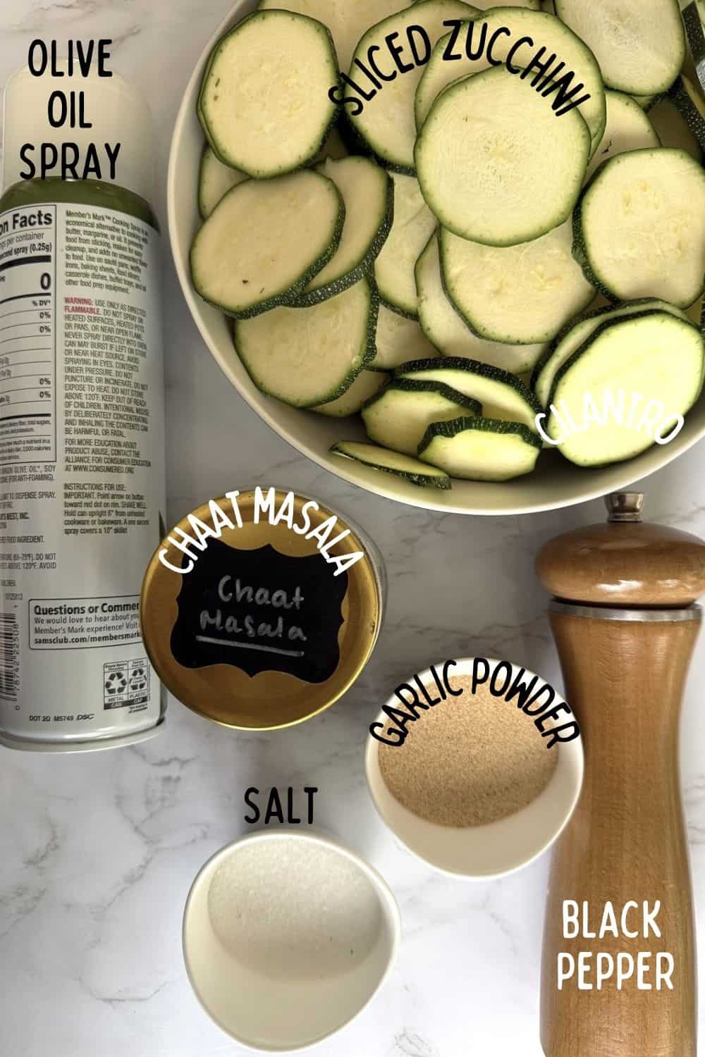 Ingredients for air-fried crispy zucchini with chaat masala recipe including sliced zucchini, salt, garlic powder, pepper, chaat masala, and olive oil spray.
