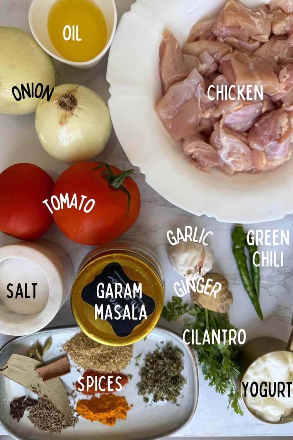 Ingredients of Easy weeknight Punjabi Chicken curry including onions, chicken, tomatoes, spices and ginger garlic and green chili on white marble background.