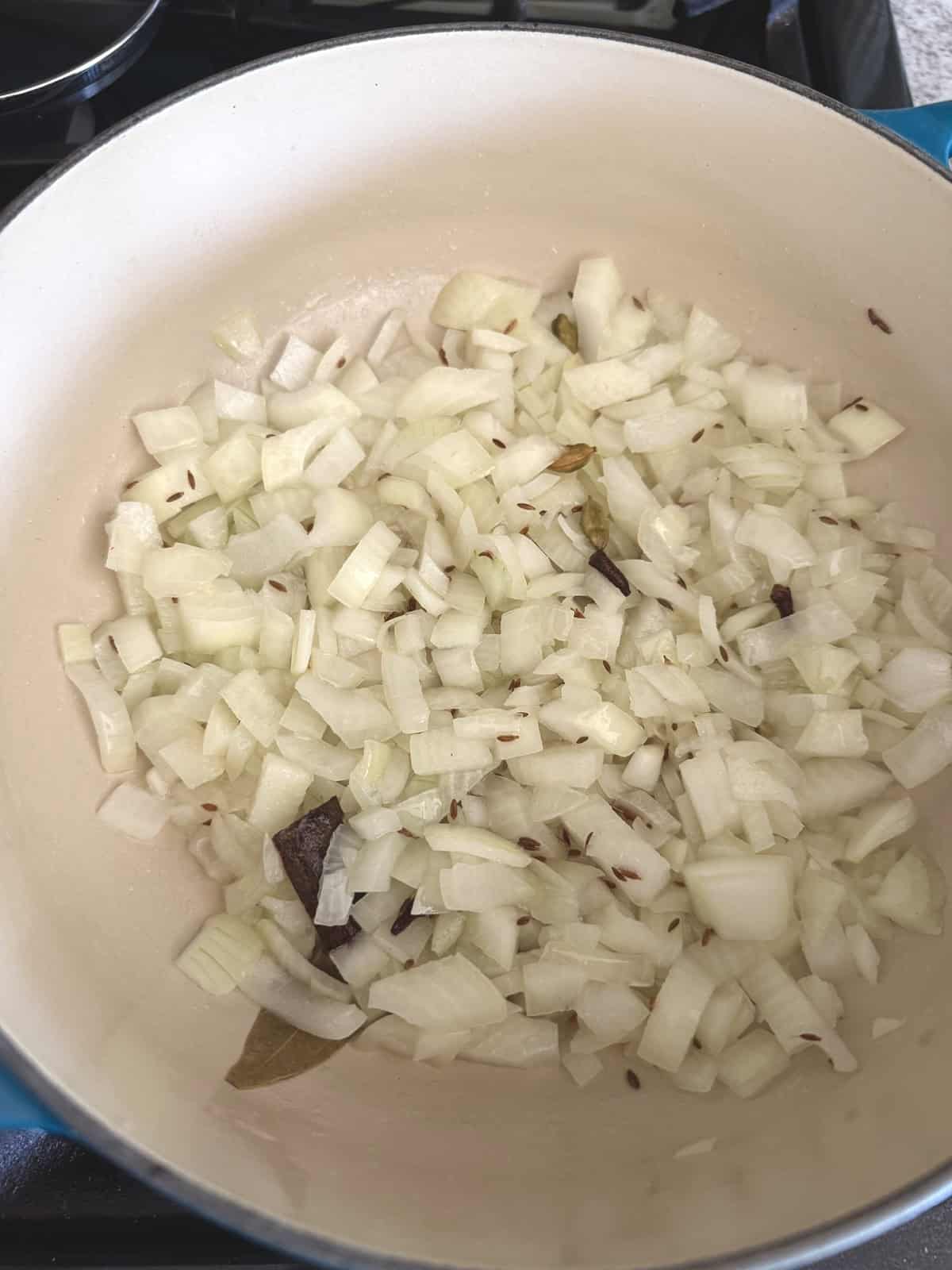 Chopped onions with whole spices in an enameled cast iron pot.