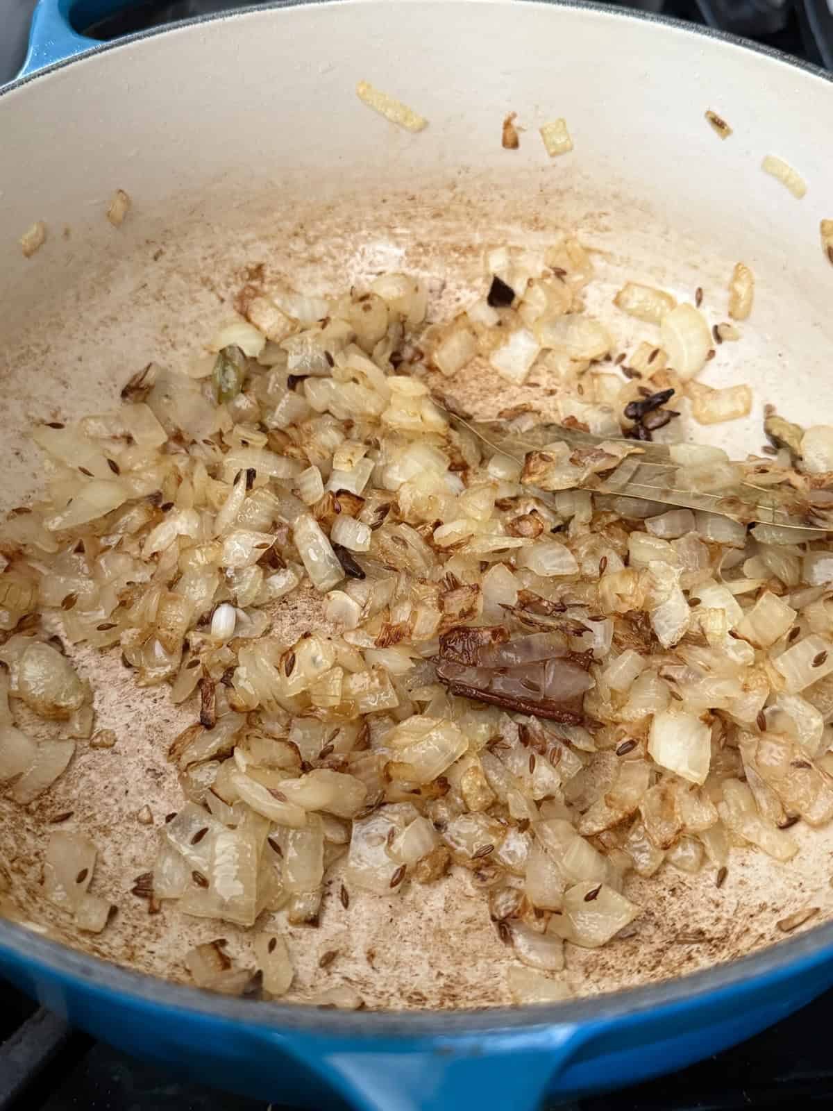 Sauteed chopped onions with whole spices in an enameled cast iron pot.