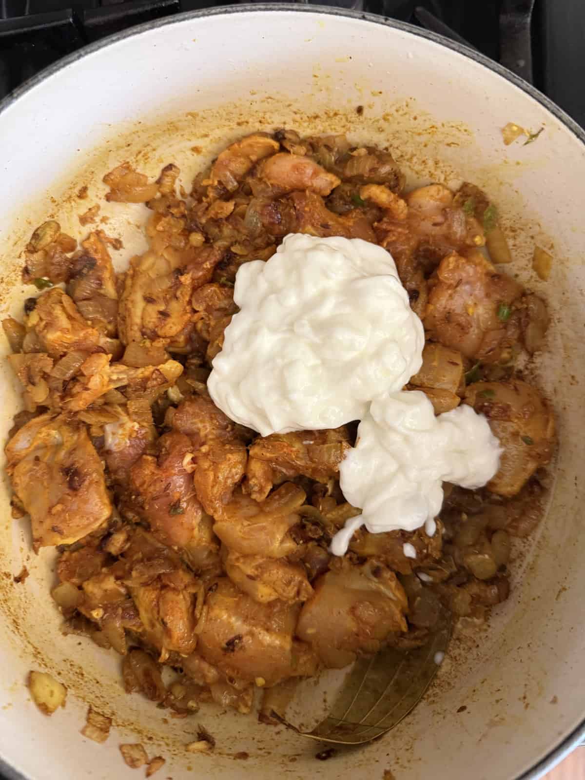 Easy weeknight punjabi chicken curry cooking in an enameled cast iron pot with yogurt.