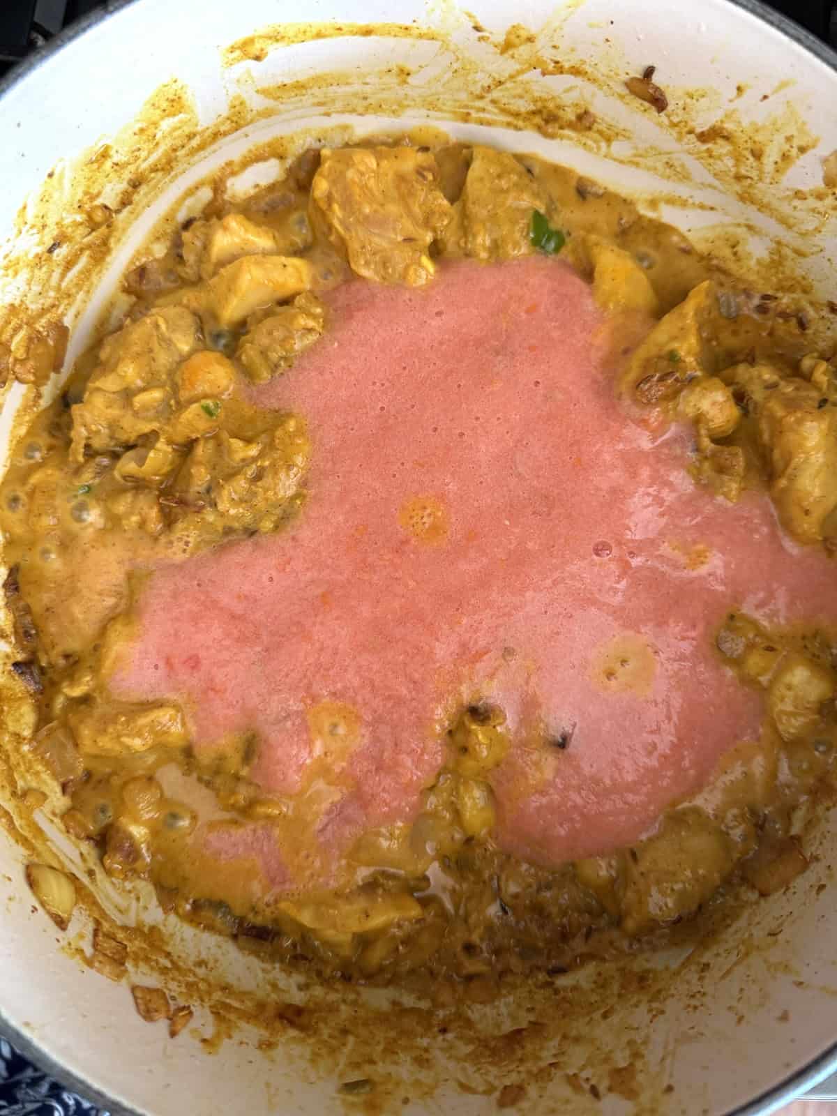 Easy weeknight punjabi chicken curry cooking in an enameled cast iron pot with tomato puree.