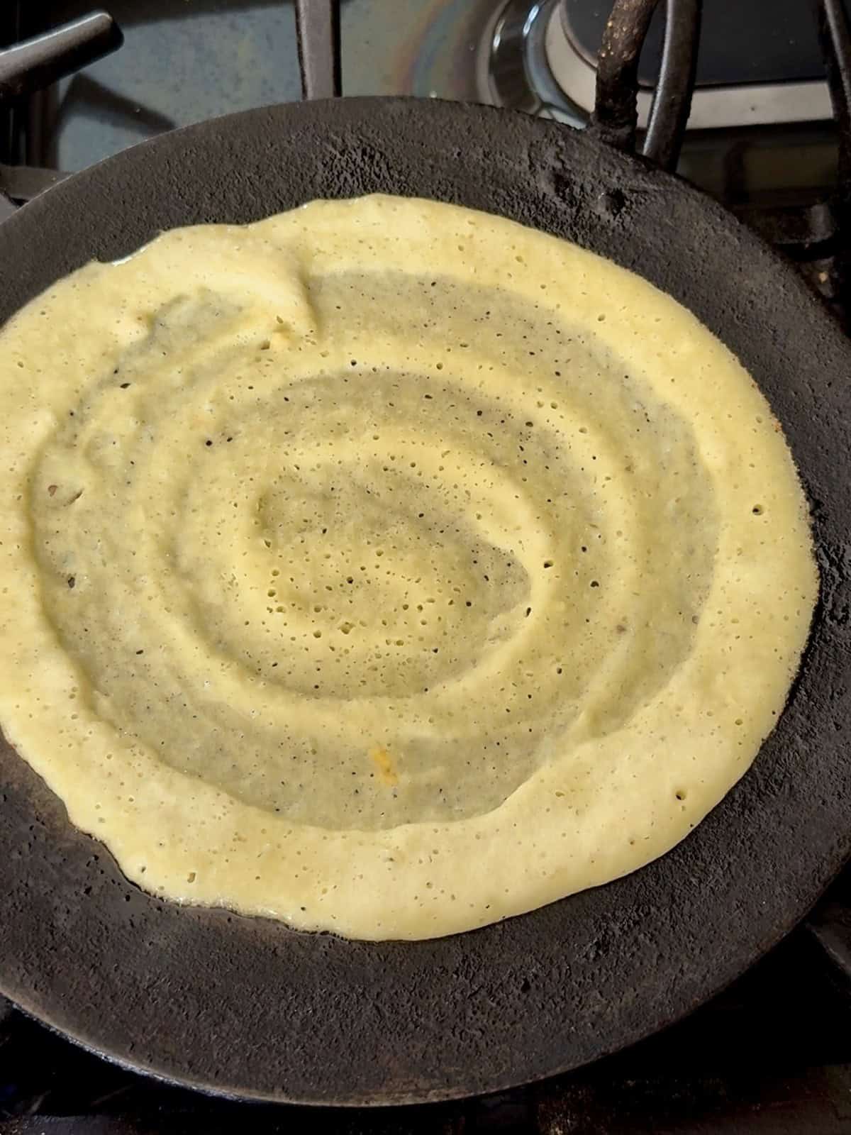 High protein moong dal cheela cooking on a cast iron skillet.