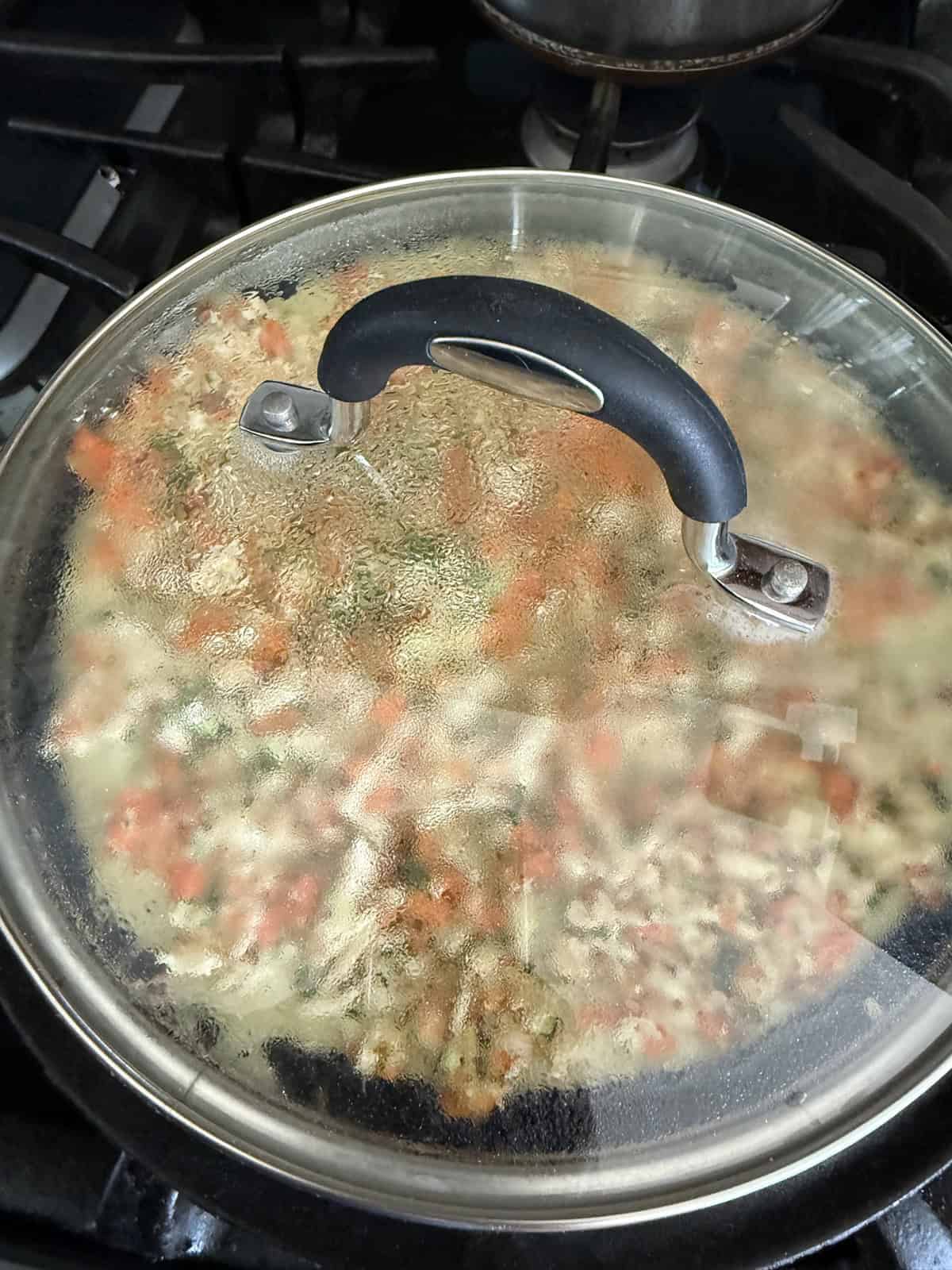 A clear glass lid on a skillet with High protein moong dal cheela with cottage cheese and tofu cooking on it.