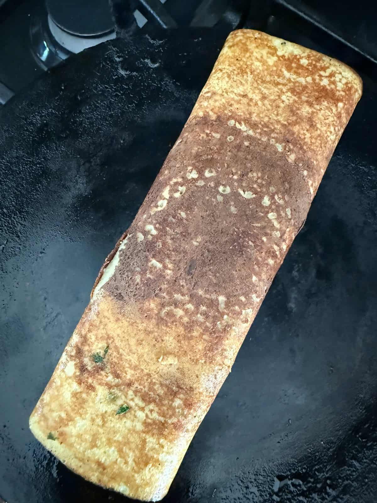 High protein moong dal cheela with cottage cheese and tofu rolled up on a cast iron skillet.